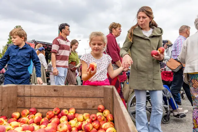 Bezoekers met kinderen bij een kist appels