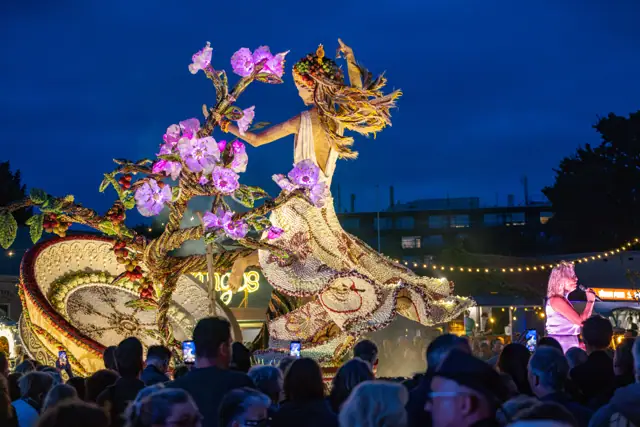 Verlicht fruitkunstwerk met bloemen en publiek in de avond