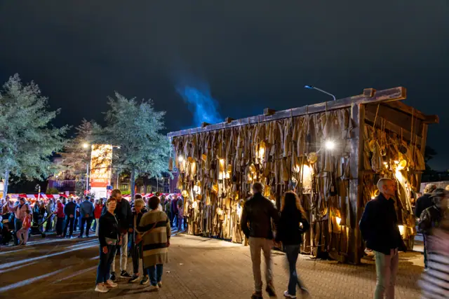 Avondsfeer met bezoekers bij een verlicht houten bouwwerk